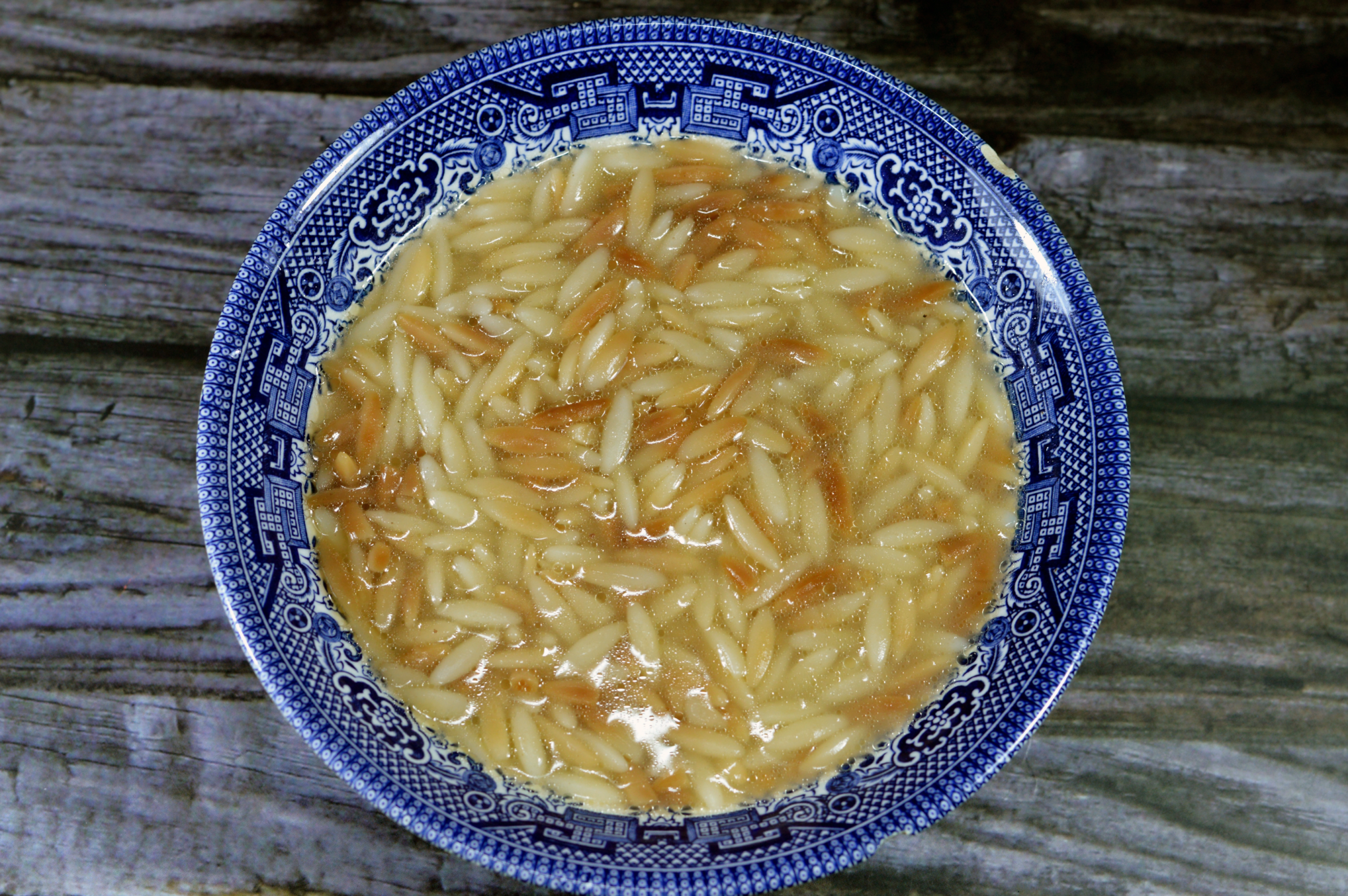 Microwaved orzo in a blue bowl with broth.