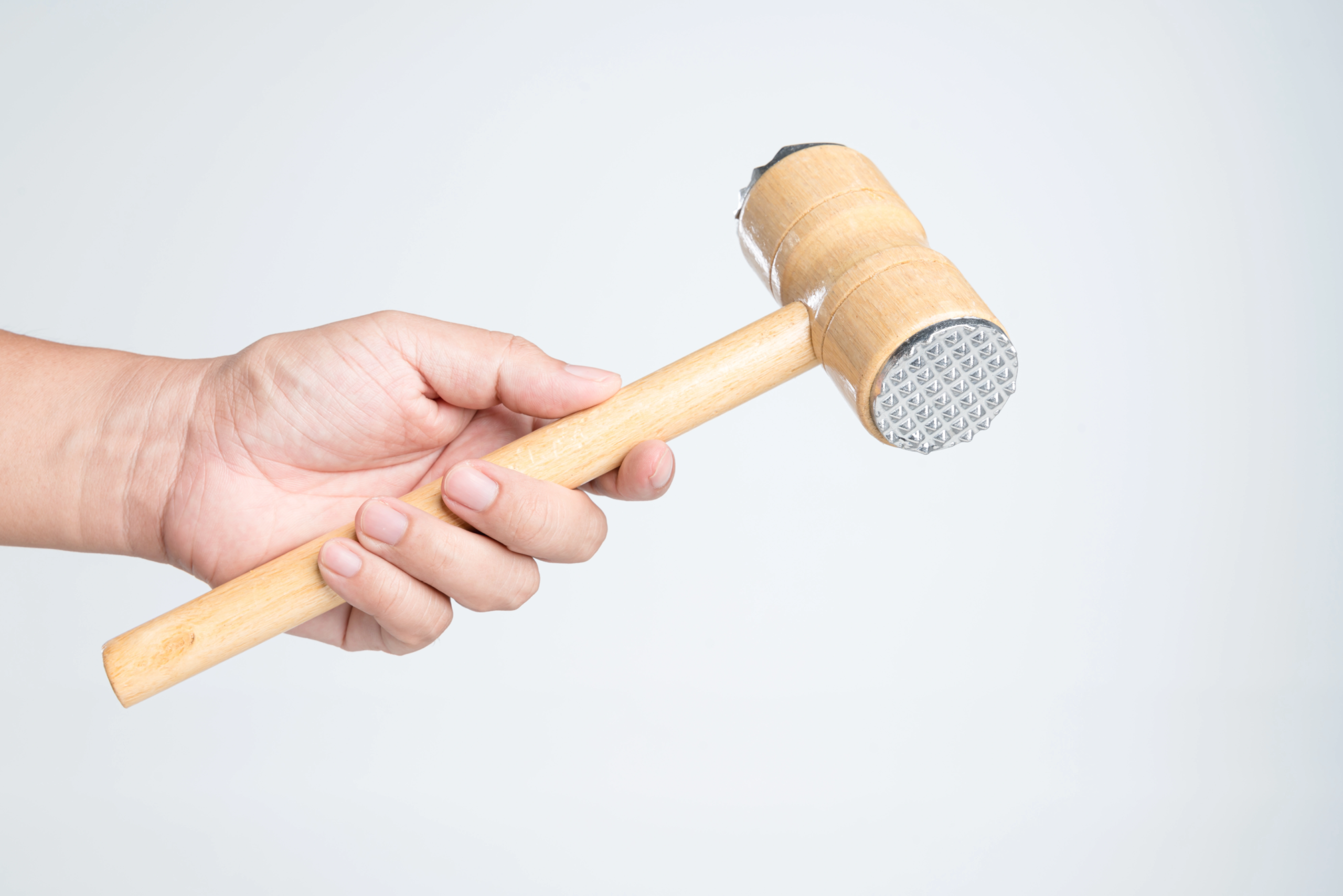 mans hand holding wooden mallet for meat with metal tips